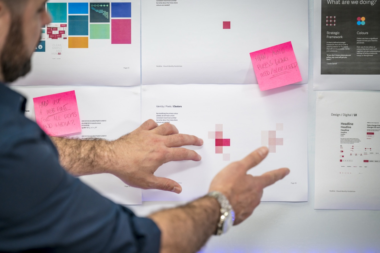 A hand moving sticky notes on a wall of brand strategy work.