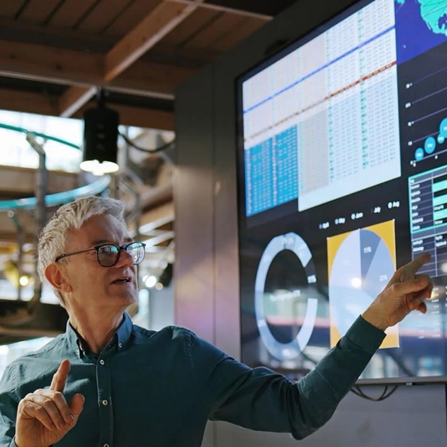 A presenter points to charts and data on a large screen.