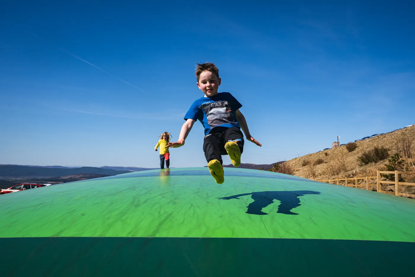 A child leaping on a green air bounce under a blue sky.