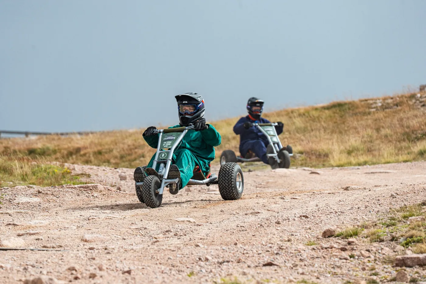 Two mountain carters in helmets racing down a gravel track.