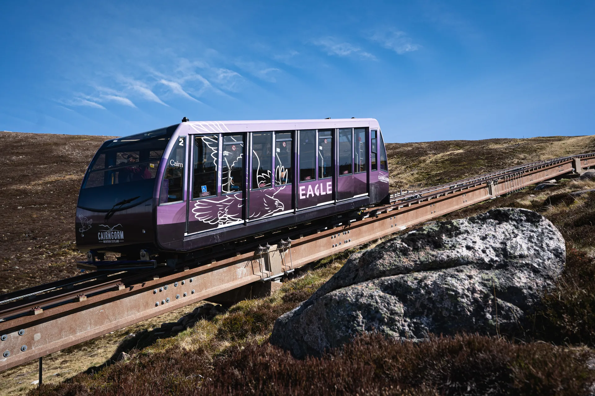 The Cairngorm funicular railway car on its track above the heather, under a blue sky.