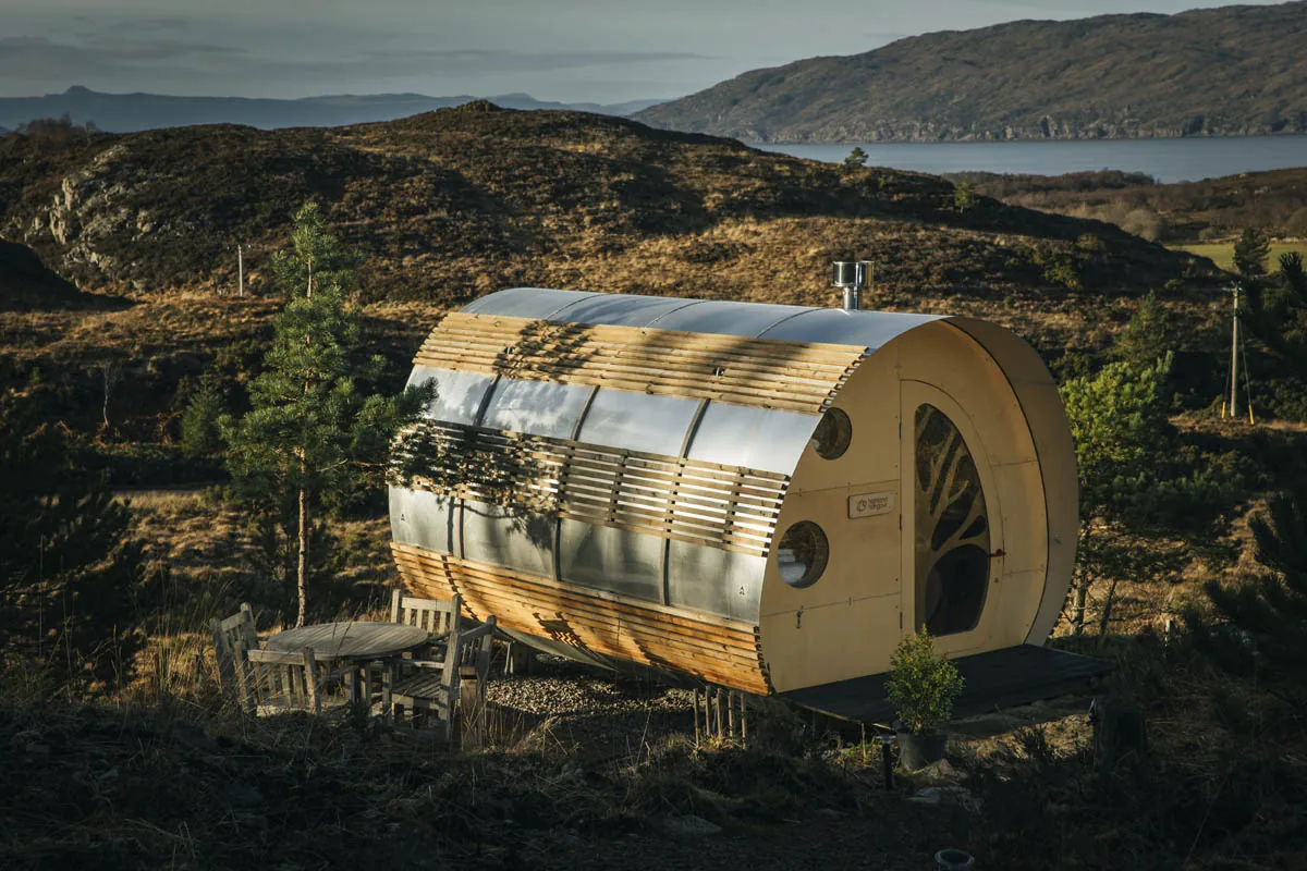 The Fuselage, a barrel-shaped timber and steel cabin on a hillside at dusk, with the sea behind.