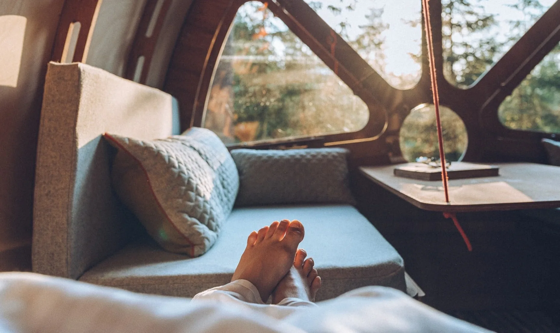 Looking out through the cabin’s round windows from a cushioned window seat, with a guest’s feet up.