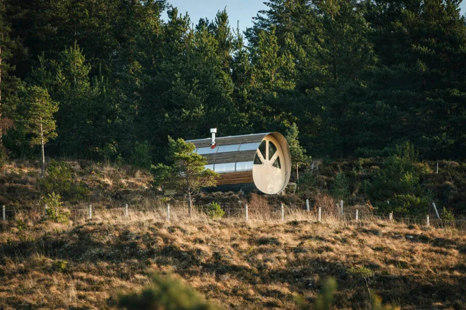 The round end of the cabin among trees on a heather hillside.