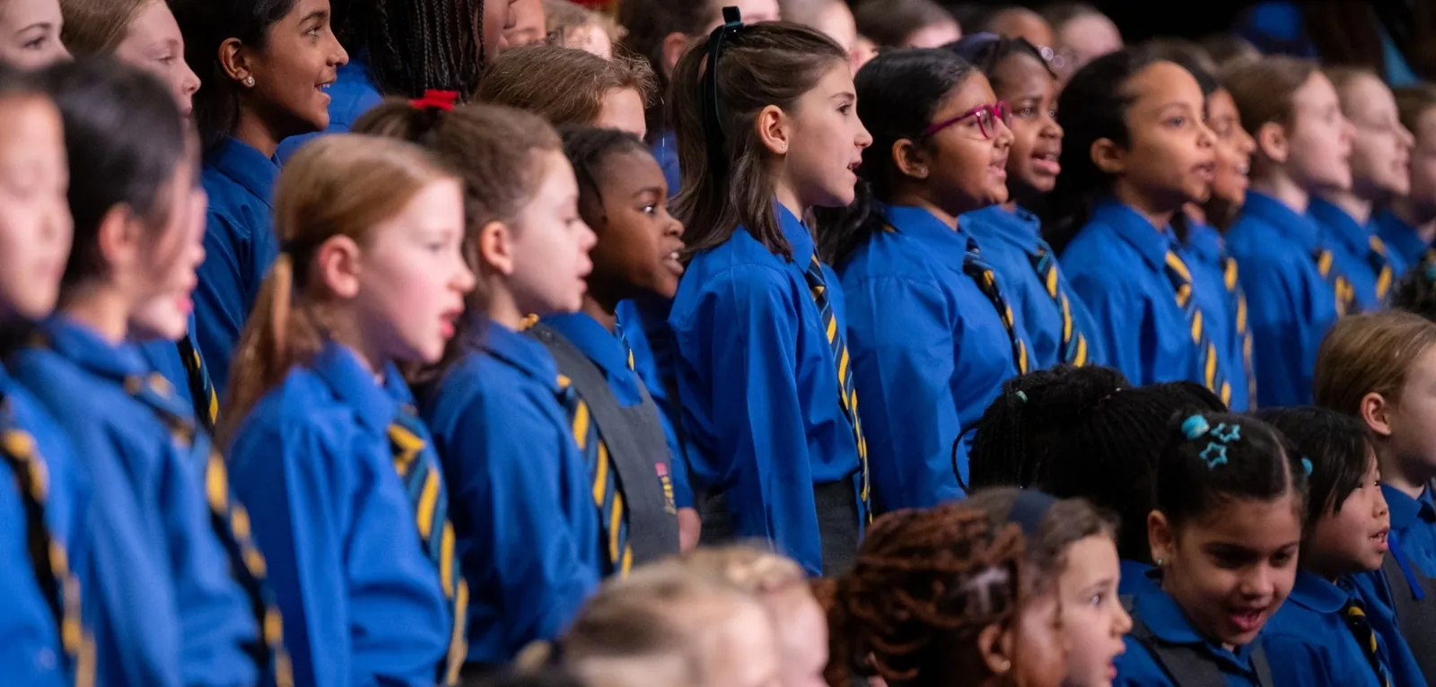 Rows of pupils in blue sweatshirts at a school concert.