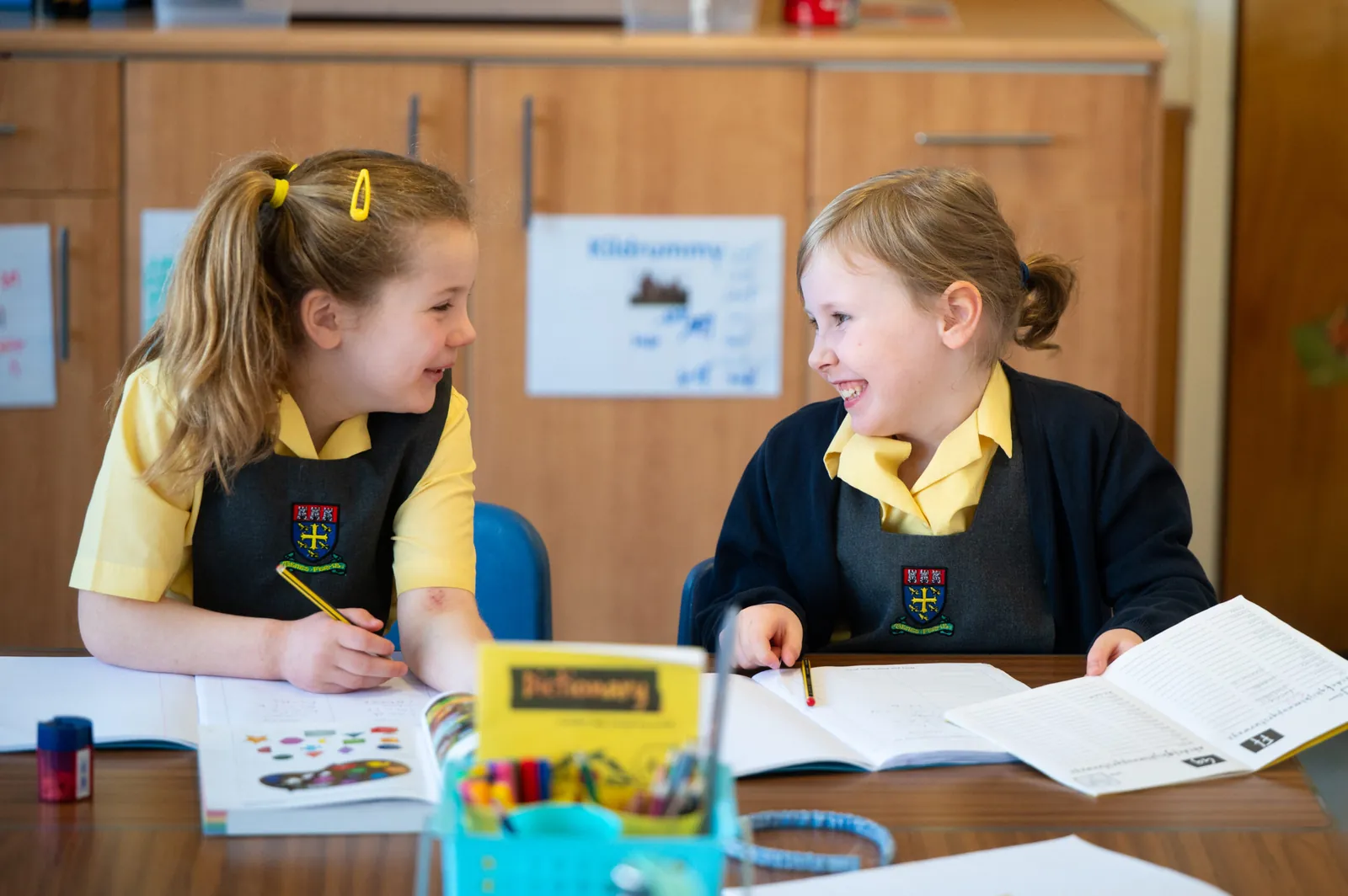 Two younger pupils sharing a book at a classroom desk.