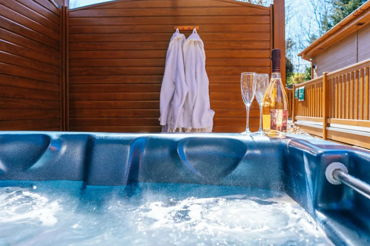 A lodge hot tub with two glasses of fizz and a bathrobe hanging beside it.