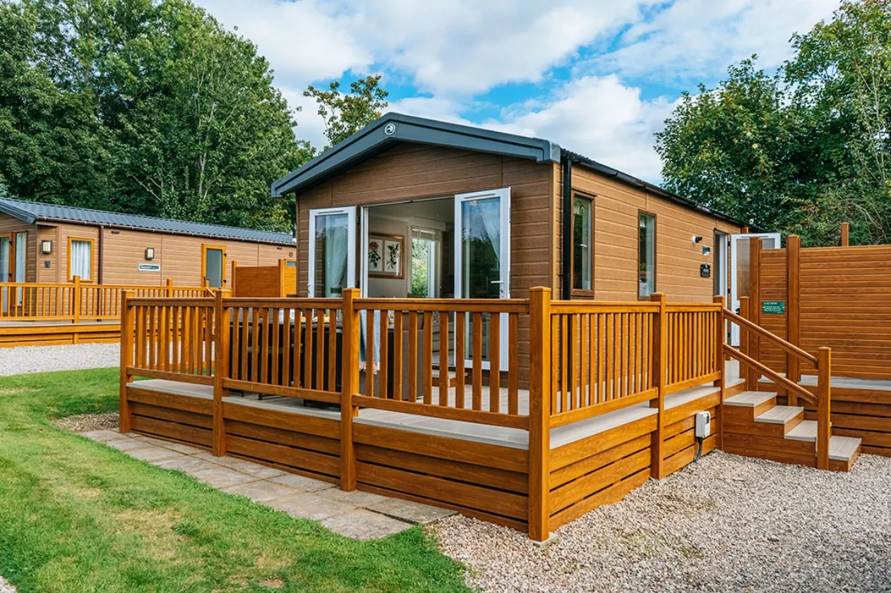 Timber lodges with decked terraces on a sunlit holiday park.